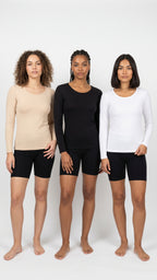 Three women standing side by side modeling long-sleeve athletic tops in beige, black, and white, paired with black bike shorts, against a plain white studio background.