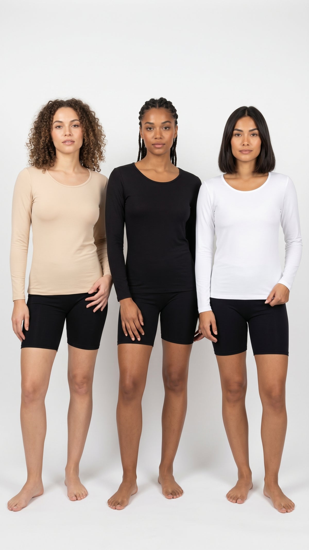 Three women standing side by side modeling long-sleeve athletic tops in beige, black, and white, paired with black bike shorts, against a plain white studio background.