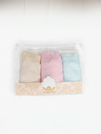 A three-pack of soft pastel-colored baby underwear in a clear plastic package with a decorative beige label. The set includes beige, light pink, and light blue pieces, with the brand name 'MYMAMONI' visible on the label.