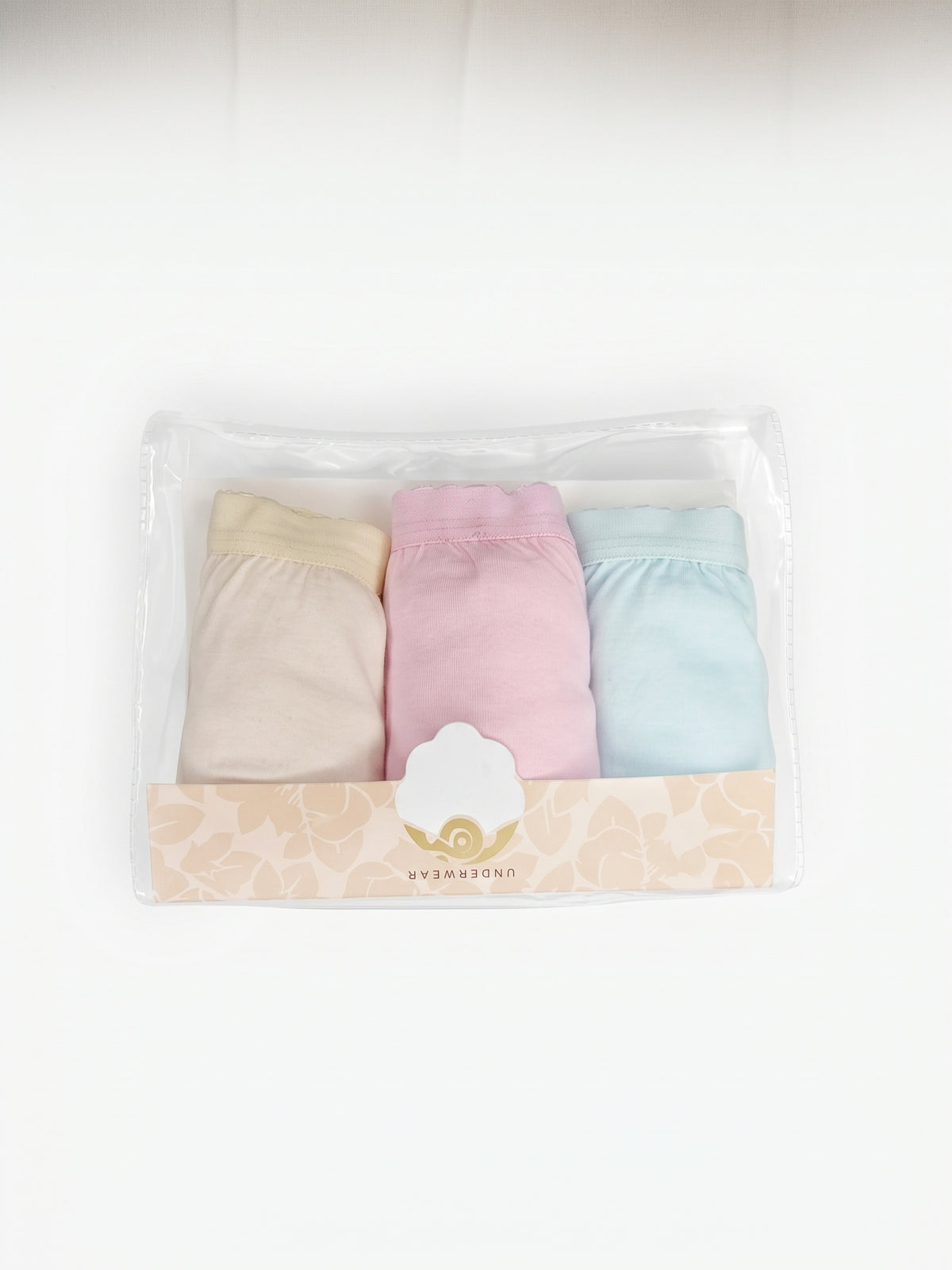 A three-pack of soft pastel-colored baby underwear in a clear plastic package with a decorative beige label. The set includes beige, light pink, and light blue pieces, with the brand name 'MYMAMONI' visible on the label.
