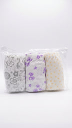 Three pairs of folded baby cloth diapers in a clear plastic bag, featuring gray floral patterns, purple flowers on white, and yellow stars on cream.