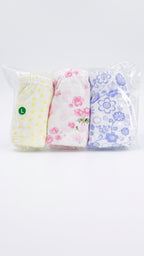 Three pairs of folded baby shorts in a clear plastic bag, featuring yellow polka dots, pink floral print, and blue floral print on white backgrounds.