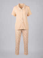 A two-piece women's pajama set displayed on a ghost mannequin against a solid gray background. The set features a short-sleeve button-up top in a light peach-beige color with white piping and a small embroidered motif on the left chest, paired with matching patterned pants in a beige and cream damask design.