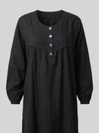 A black long-sleeve dress with a round neckline, three front buttons, and a gathered chest detail, shown against a solid gray background.