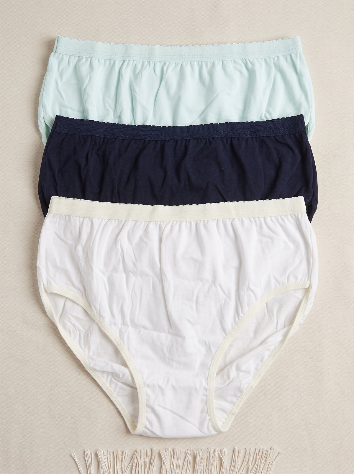 A three-pack of women's underwear in a clear plastic clamshell package with a beige paper band. The pack contains a cream-colored pair, a dark navy pair, and a light blue pair, with a central white label showing a gold logo and the word 'UNISEX'.